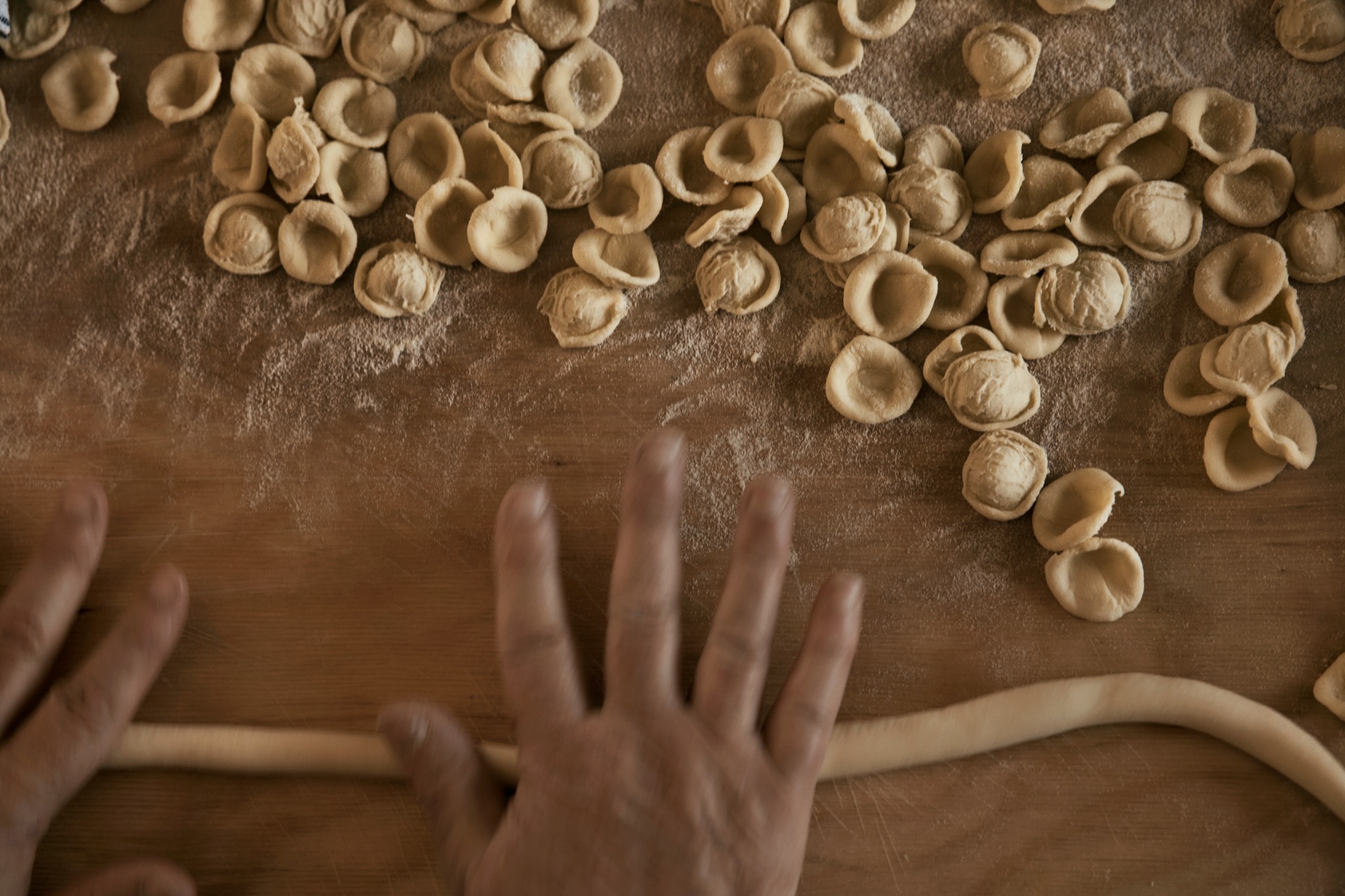 Hands making fresh orecchiette pasta on a floured wooden board