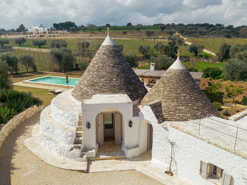 Traditional conical roofs of Trullo Petrarolo with the pool and countryside beyond